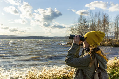 Young woman looking through binoculars at birds on the lake. birdwatching, zoology, ecology research