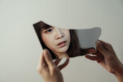 Cropped hands of woman holding mirror against wall