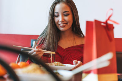 Asian woman in red clothes eating noodles with bamboo chopsticks in chinese vietnamese restaurant