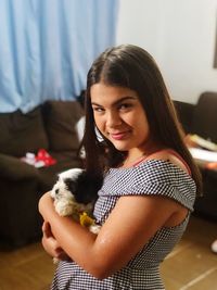 Portrait of girl holding dog while standing at home