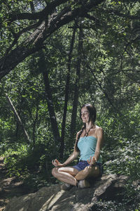 Portrait of young woman sitting on tree in forest