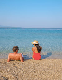 Rear view of woman relaxing at beach against clear sky
