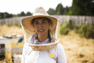 Portrait of female beekeeper wearing protective mask and hat on field