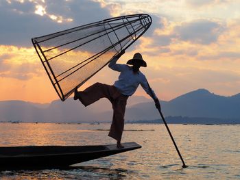 Low angle view of man fishing in sea against sky during sunset