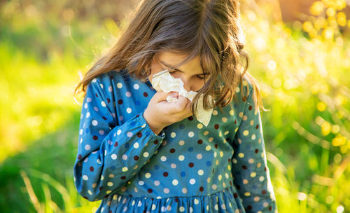 Girl holding flower blowing nose with tissue