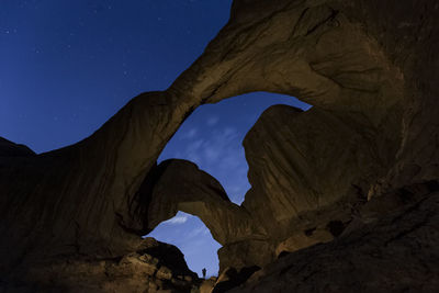 Silhouette of hiker framed by double arch under starry sky in arches