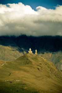 Gergeti trinity church on mountain against cloudy sky