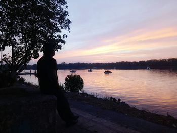 Silhouette woman standing by retaining wall against lake during sunset