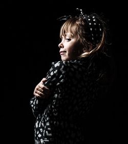 Girl looking away while standing against black background