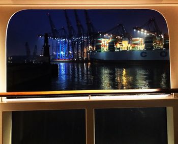 Illuminated harbor by sea against sky at night