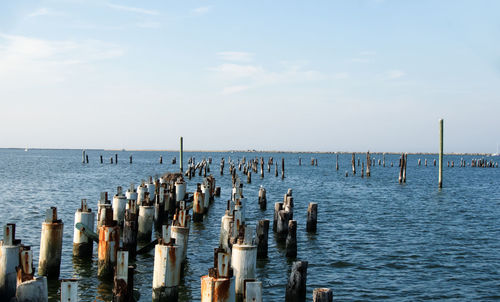 Wooden posts in sea against sky