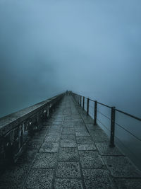 Empty footpath by railing against sky