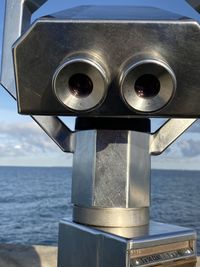 Close-up of coin-operated binoculars by sea against sky