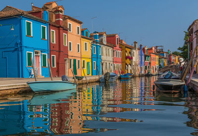 Boats moored in canal by houses against sky