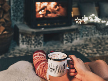 Personal perspective of woman relaxing on sofa by fireplace. holding cocoa.