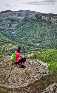 Woman sitting on rock against mountains