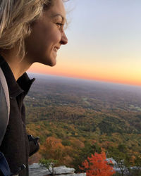 Woman looking at cityscape against sky during sunset