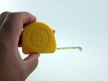 Close-up of hand holding yellow flower against gray background