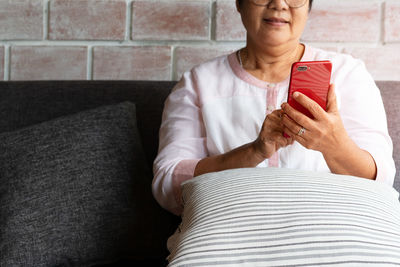 Senior woman using mobile phone while sitting on sofa at home