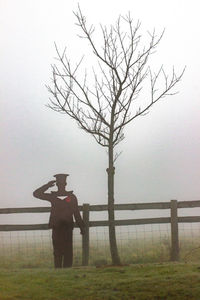 Man standing by bare tree in foggy weather