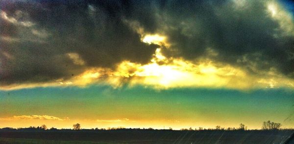 Scenic view of landscape against cloudy sky at sunset