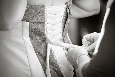 Cropped hands of woman assisting bride in dressing up