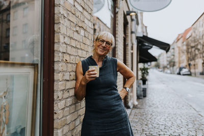 Portrait of smiling saleswoman with coffee cup standing outside store
