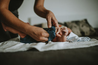 Cropped image of mother changing diaper of son on bed at home