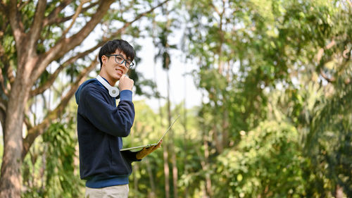 Side view of young man standing against trees