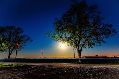 Road by illuminated street against blue sky at night