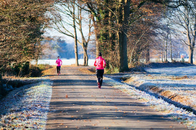 Rear view of woman running on road amidst trees