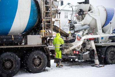 Rear view of man working while standing by cement mixer on snow covered field