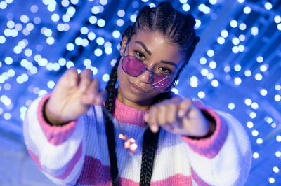 Cheerful black woman with braided hairstyle and pink glasses enjoying christmas lights