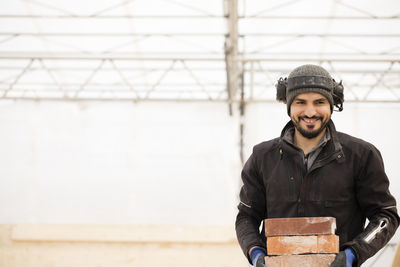 Portrait of happy male construction worker carrying bricks