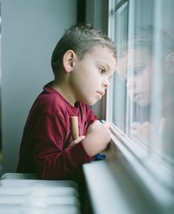 Thoughtful boy looking through window at home