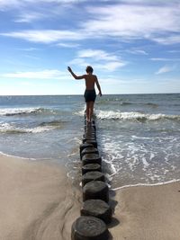 Rear view of shirtless boy walking on wooden posts at beach