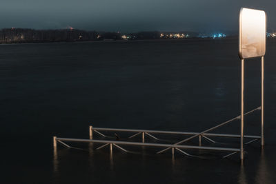 Illuminated railing by sea against sky at night