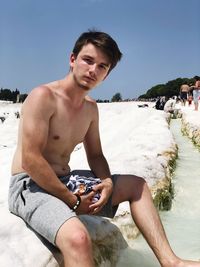 Portrait of shirtless young man sitting at beach