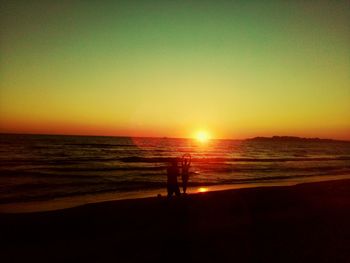 Silhouette people standing on beach at sunset