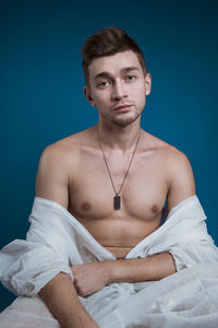 Portrait of young man sitting on bed against blue background
