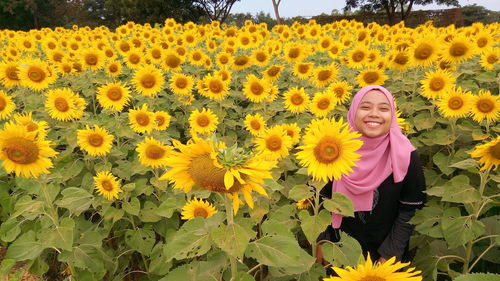 Portrait of smiling woman wearing hijab while standing amidst sunflower field