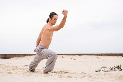 Full length of young man exercising at beach against clear sky