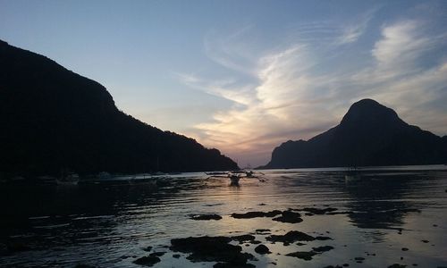 Scenic view of silhouette mountains at beach against sky during sunset