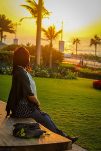 Rear view of woman sitting at park during sunset