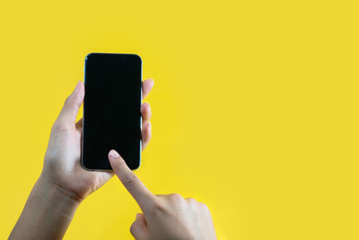 Low section of person holding smart phone against yellow background