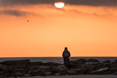 Silhouette man standing on rock by sea against sky during sunset