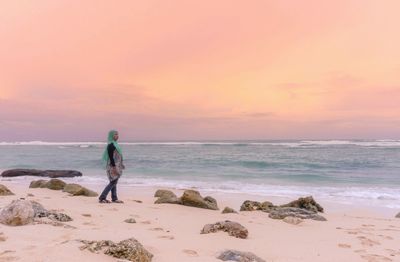 Side view of woman standing on shore at beach against sky during sunset