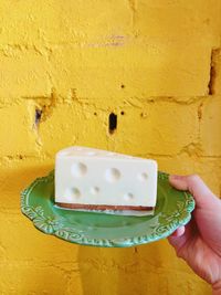 Midsection of person holding ice cream against yellow wall