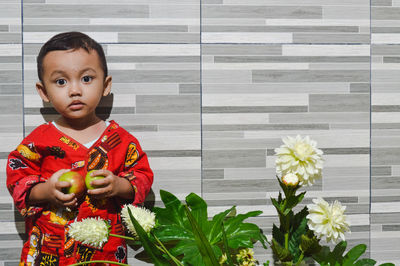 Portrait of boy holding fruit standing against wall