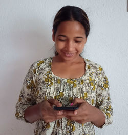 Young woman using mobile phone against wall